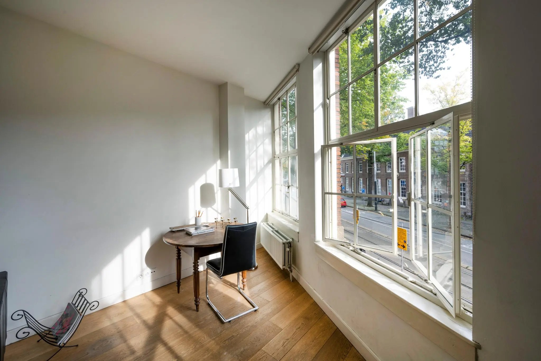 Licht thuiskantoor met houten vloer en groot open raam met uitzicht op de Nieuwezijds Voorburgwal in Amsterdam.